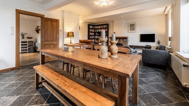 A spacious living area with a wooden dining table, benches, a fireplace, a bookshelf, and a television. - Holiday Home in South Limburg With a Terrace (Klimmen)