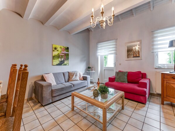Een woonkamer met een grijze bank, een rode bank, een glazen salontafel en een kroonluchter.