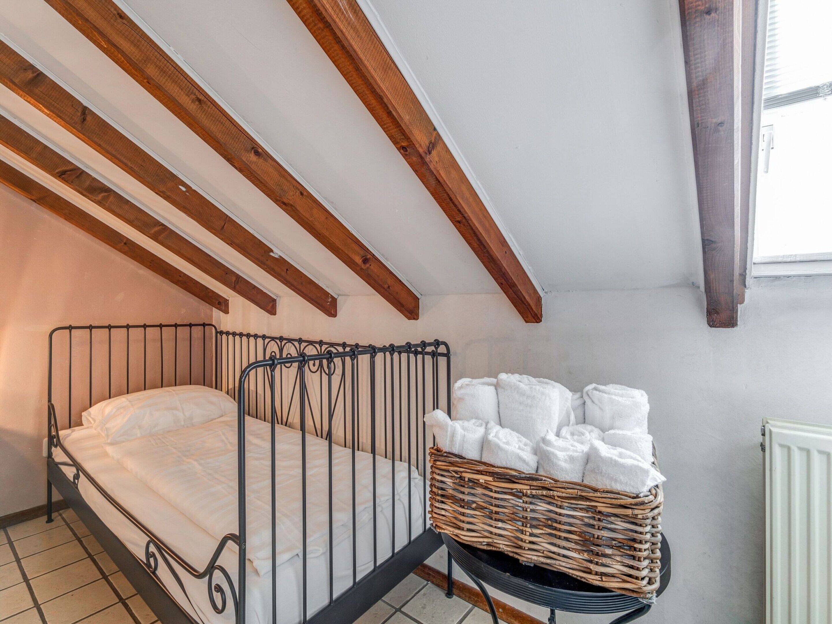 Ein kleines, gemütliches Zimmer mit einem Einzelbett, einem Korbwäscheschrank mit Handtüchern und einem Fenster mit Jalousien.