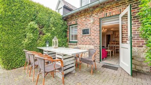 Une terrasse avec une table et des chaises, un mur en briques et une haie.