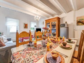 Een gezellig eetgedeelte met een lange tafel gedekt voor het ontbijt, een houten kast met glazen deuren, en een televisie op de achtergrond.