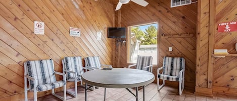 Un intérieur en bois avec une table ronde et quatre chaises à rayures, un ventilateur de plafond et un panneau indiquant « Trousse de premiers secours ».