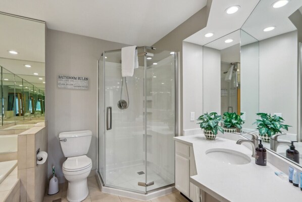 Un baño moderno con cabina de ducha de vidrio, inodoro y zona de lavabo con plantas y artículos de aseo.