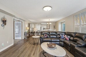 A modern living room with a leather sectional sofa, a round coffee table, and a dining area in the background. - Home Sweet Getaway - Perfect for Girl's Trips & Families (Wisconsin Dells)