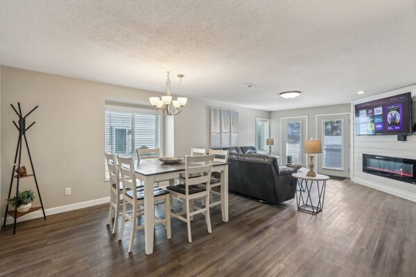 A spacious living room with a dining area, a fireplace, and a television mounted on the wall.