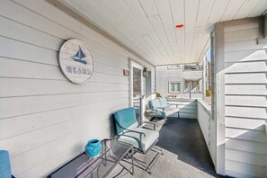 Un espacio de estar al aire libre techado con sillas de metal y una mesa, un cartel con un velero y texto, y vistas de un edificio con ventanas.