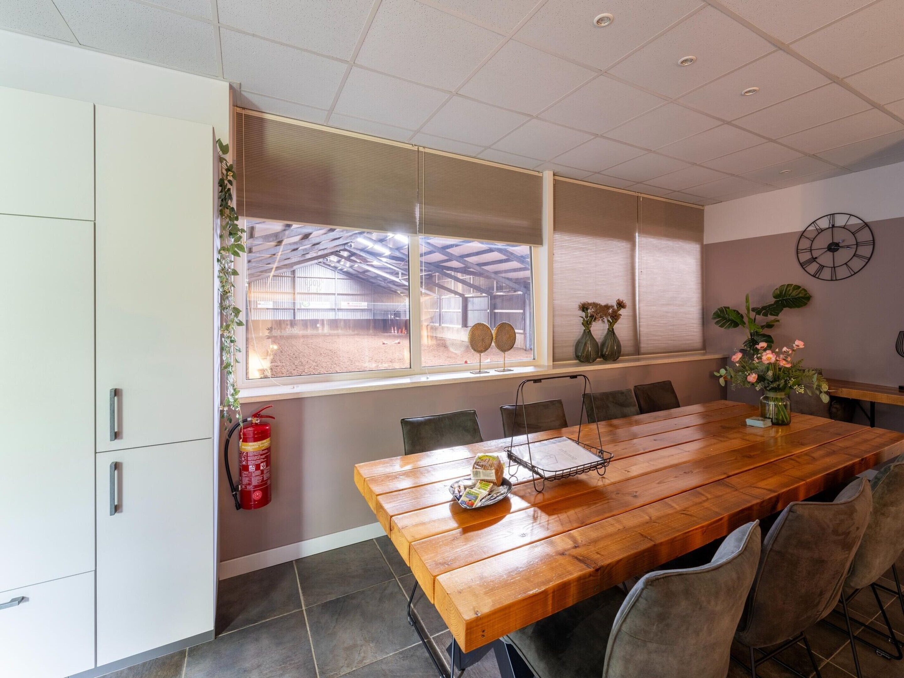 A dining area with a wooden table, chairs, a fire extinguisher, and a window with a view of an outdoor area.