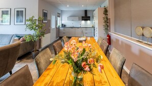 Une cuisine moderne avec des meubles blancs, une table à manger en bois avec des chaises et un vase de fleurs.