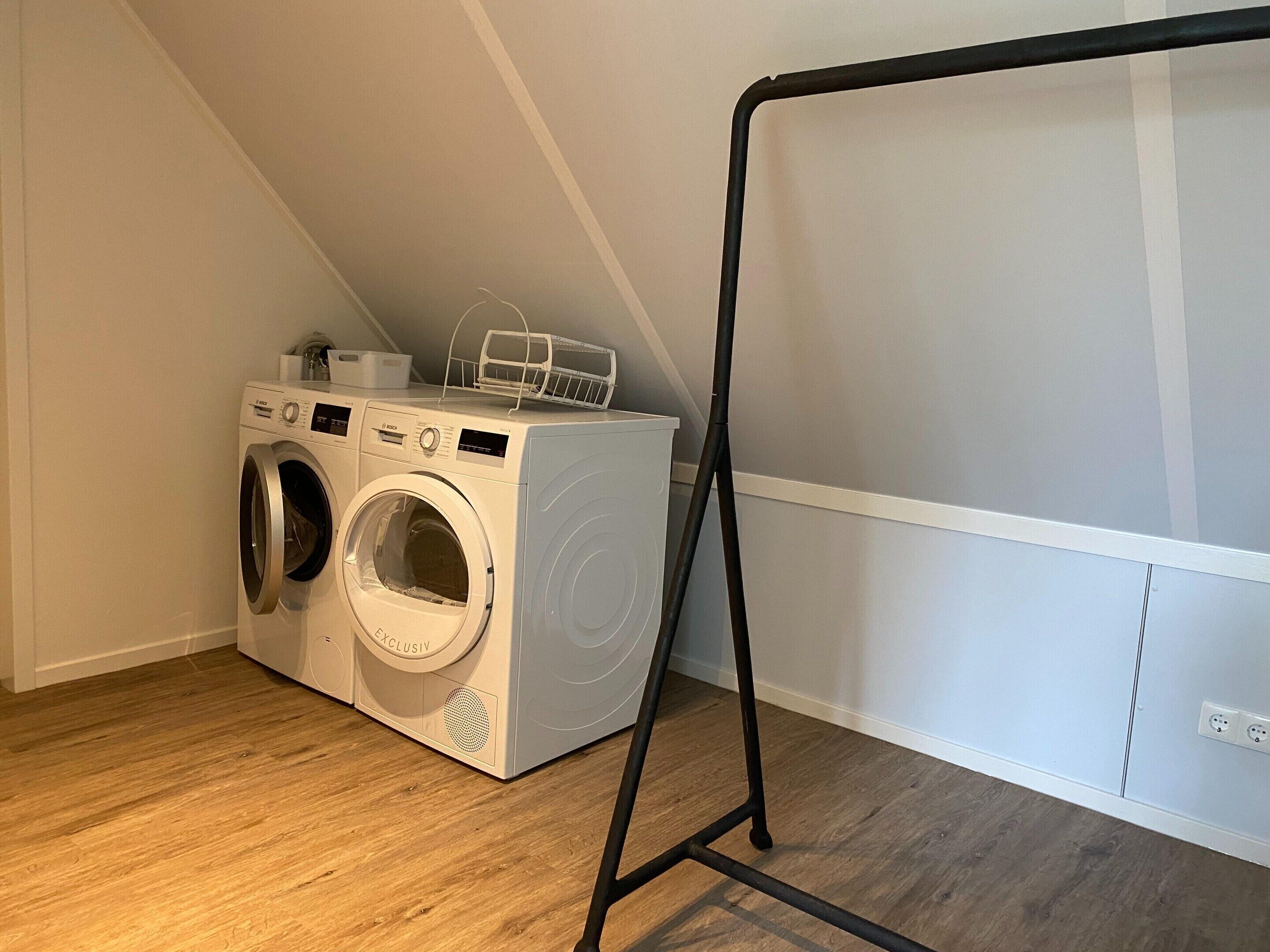 A laundry area with two front-loading washing machines and a drying rack.
