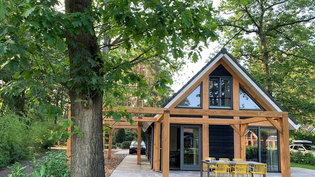 A modern house with a wooden exterior, large windows, and a patio area with yellow chairs. - Holiday Home in Lochem With Garden View (Lochem)
