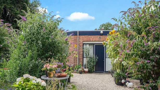 Un giardino con un sentiero sterrato che conduce a un edificio in mattoni con una porta scura.