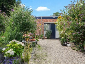 Un giardino con un sentiero sterrato che conduce a un edificio in mattoni con una porta scura.
