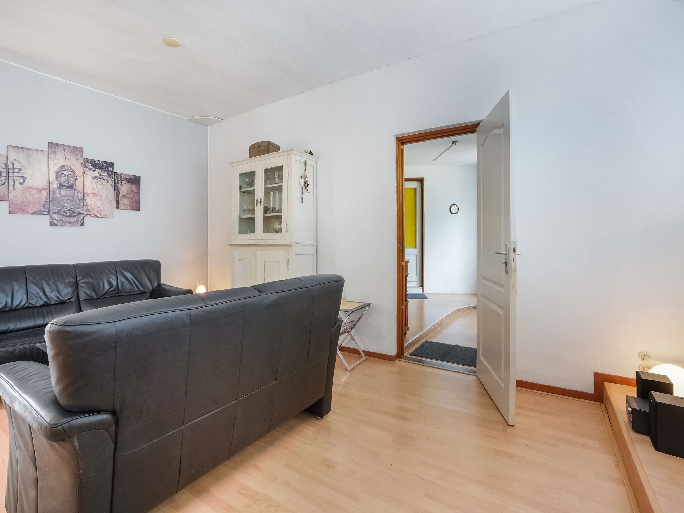 A living room with a dark leather sofa, a cabinet with glass doors, and a wooden floor.