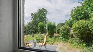 Vista dalla finestra su un giardino con tavolo e sedie da patio, circondato da vegetazione lussureggiante e alberi.