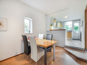 A dining area with a wooden table and chairs, a kitchen with cabinets and a window, and a door leading outside. - Bungalow in Landgraaf With Terrace (Landgraaf)