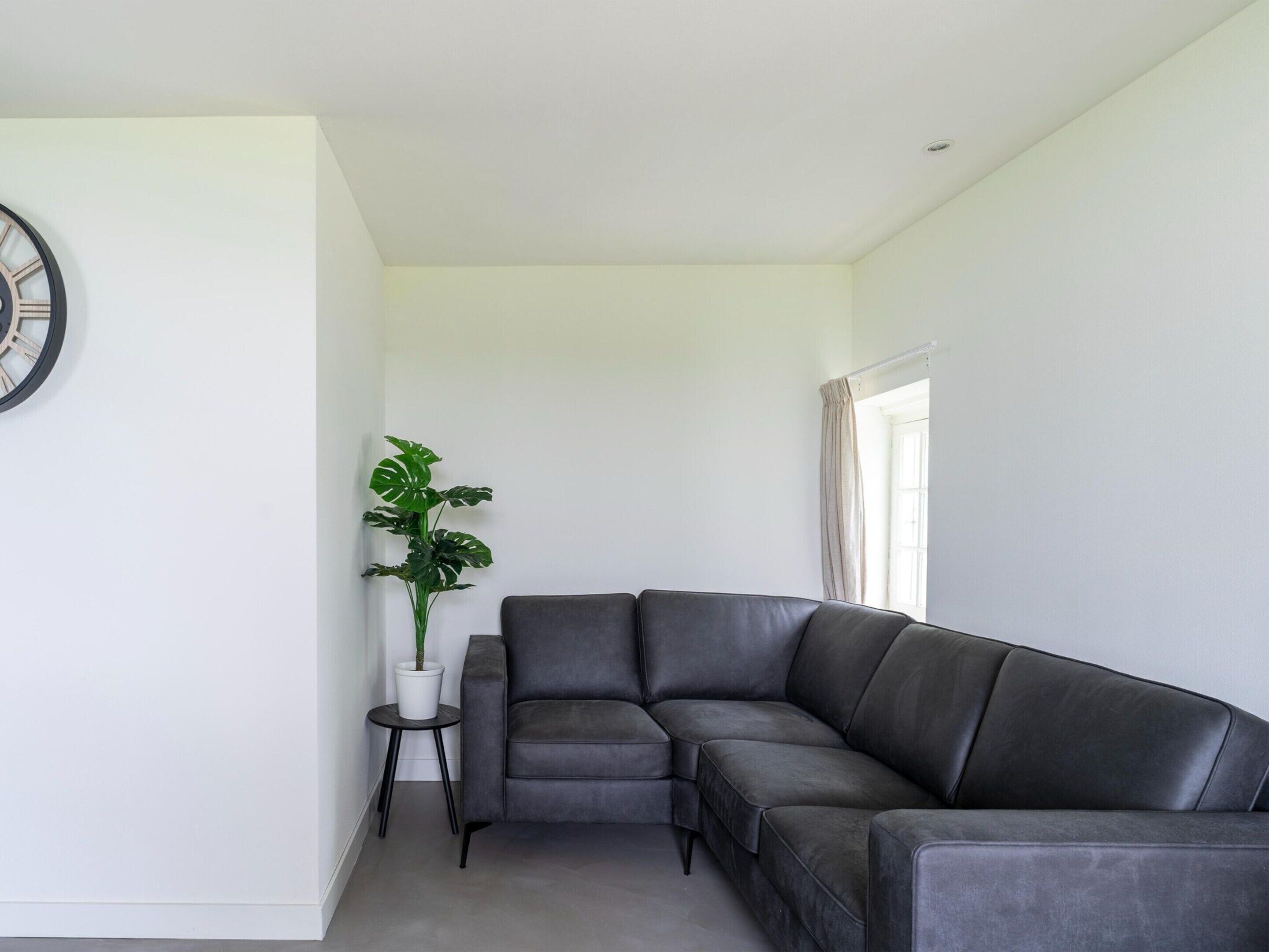 A modern living room with a grey leather sofa, a potted plant, and a minimalist design.