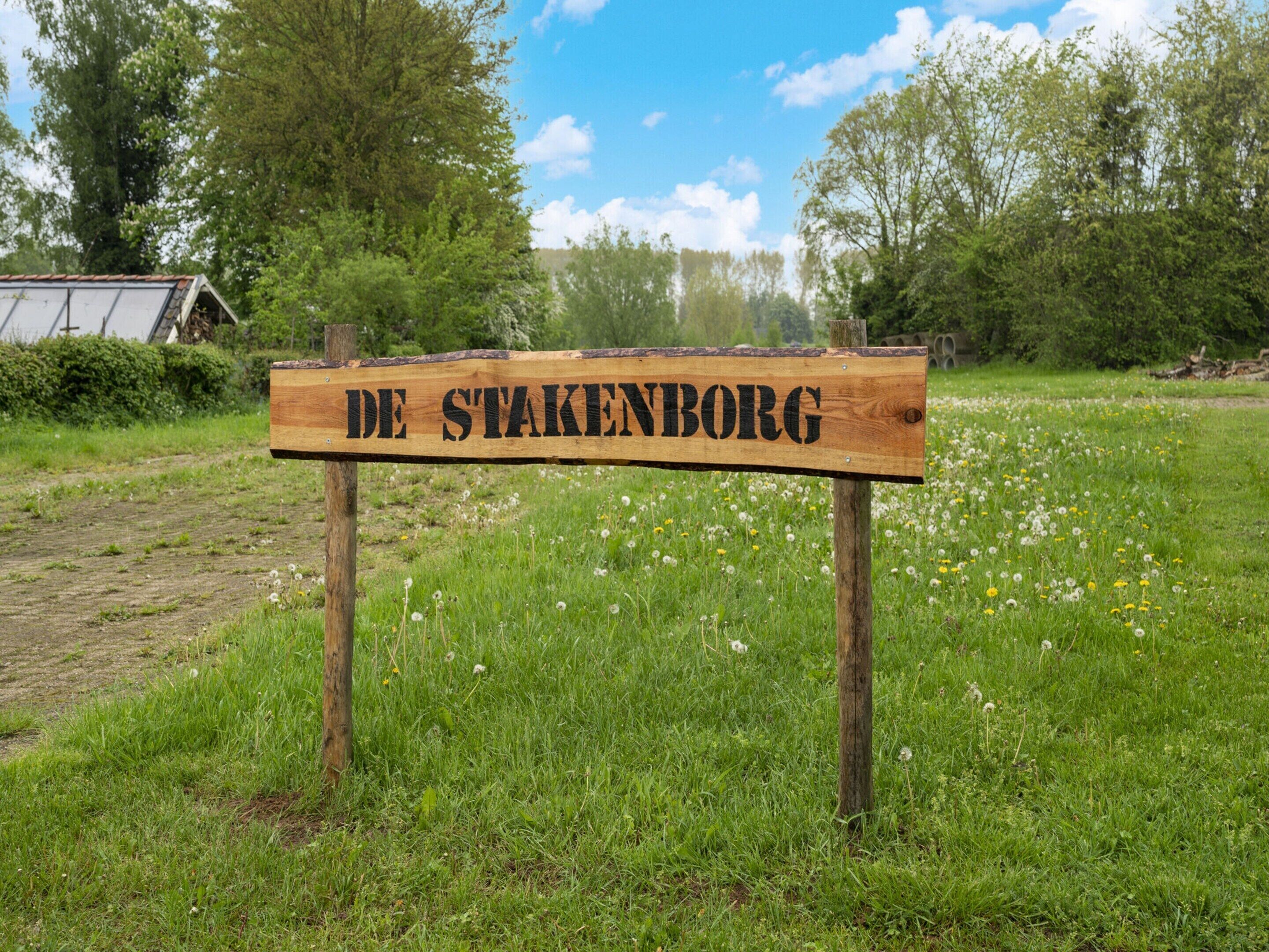 A wooden sign with "DE STAKENBORG" written on it, set in a grassy field with trees in the background.