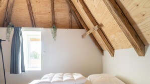 A bedroom with a sloped wooden ceiling, a bed with white bedding, a window with a curtain, and a small plant on the wall. - Comfortable Holiday Home in Voorst With Garden (Voorst)