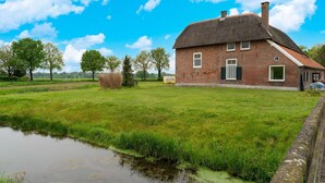 A brick house with a thatched roof, a grassy field, and a canal. - Comfortable Holiday Home in Voorst With Garden (Voorst)