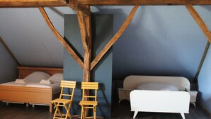 Une chambre avec un plafond en pente, des poutres en bois, un lit, deux chaises et une table de chevet.