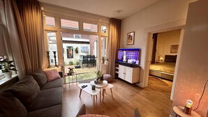Un salon avec un canapé, une table basse et un téléviseur. Il y a un balcon avec une table et des chaises.