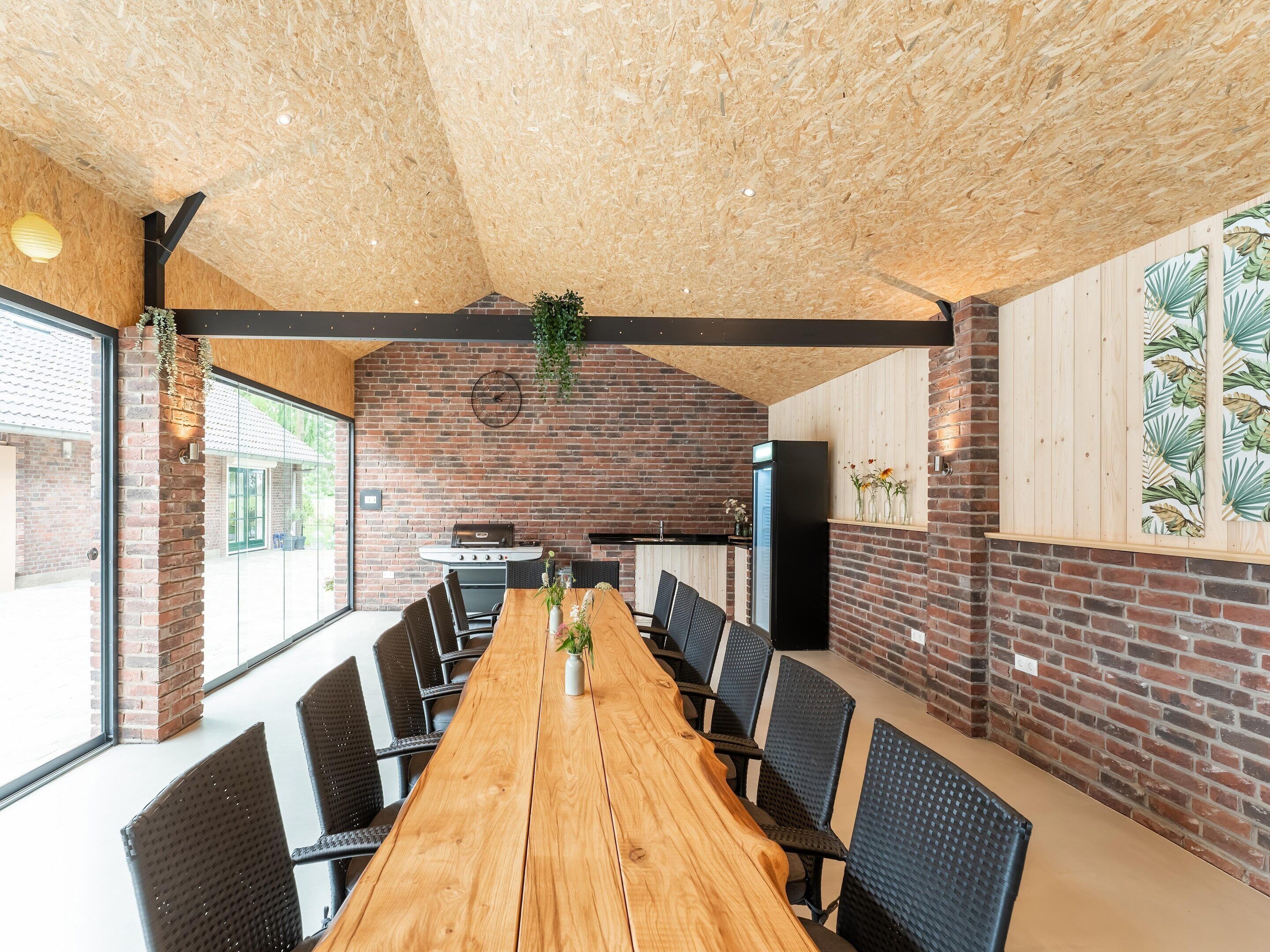 Ein langer Holztisch mit schwarzen Stühlen, eine Ziegelwand und eine hängende Pflanze.
