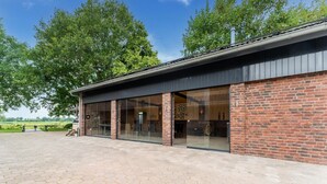 A building with large glass doors, a brick facade, and a paved area in front. - Farmhouse in the Achterhoek With hot tub and Beach Volleyball (Megchelen)