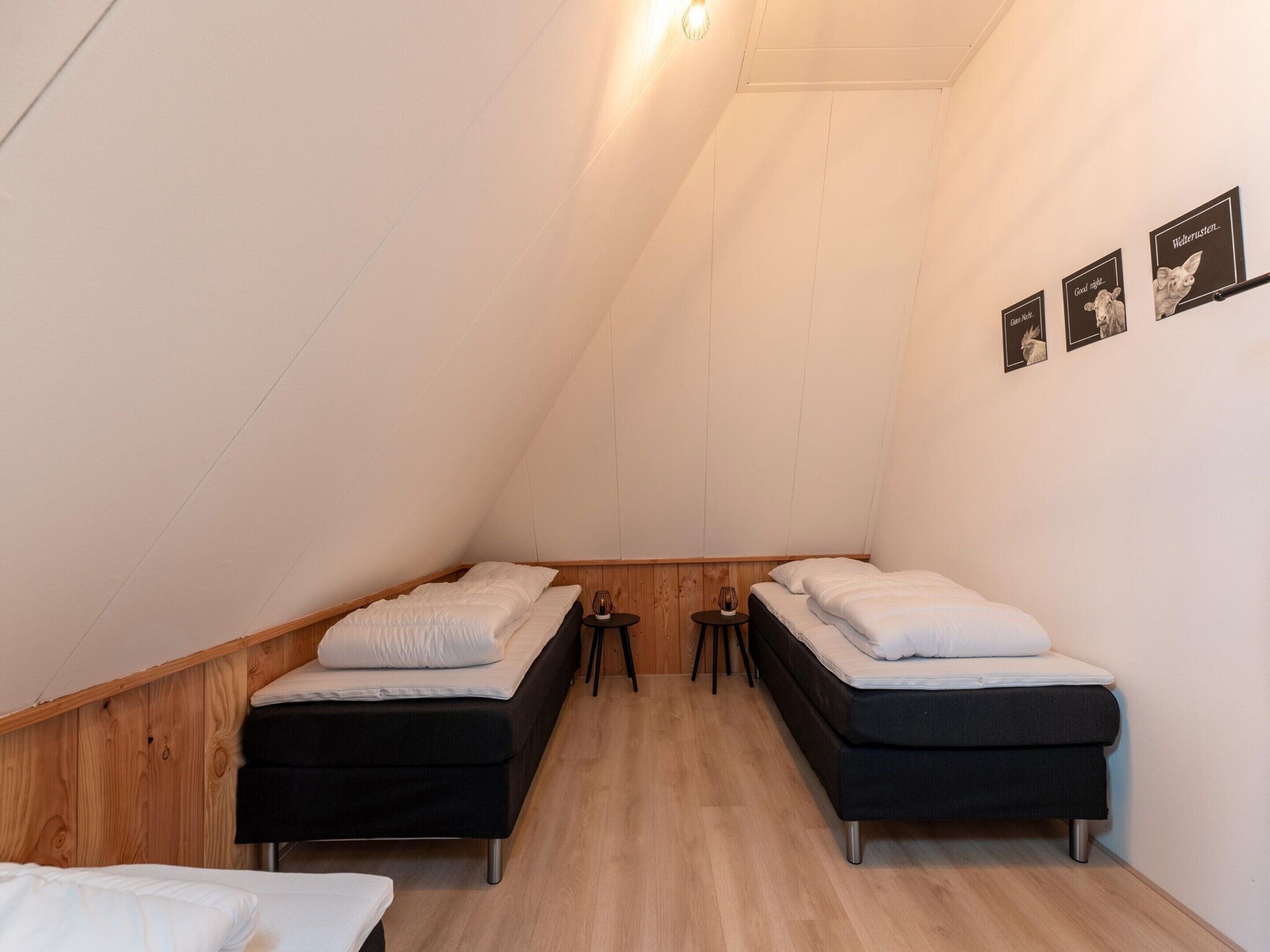 A dormitory room with two beds, wooden walls, and a sloped ceiling.