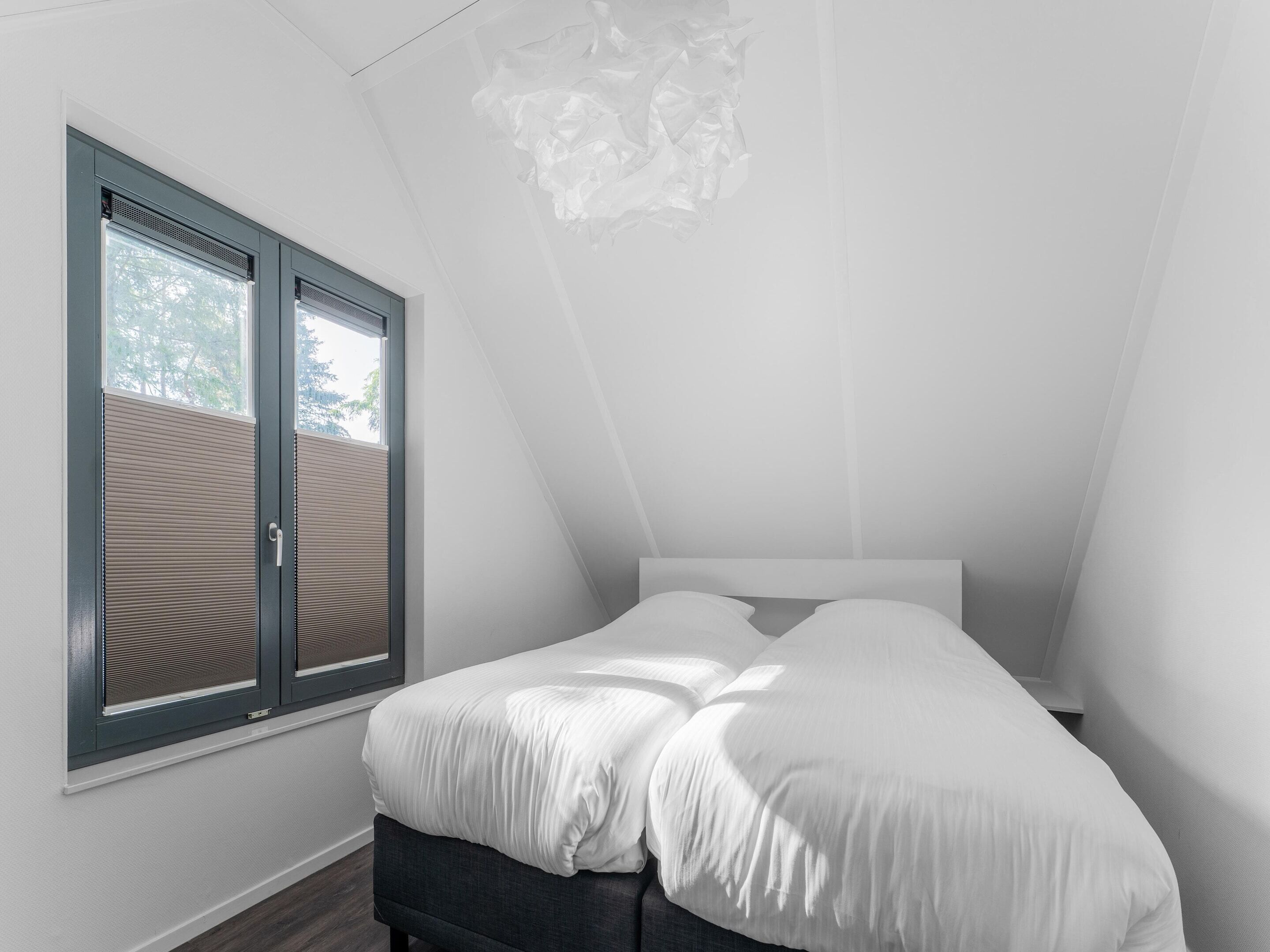 A bedroom with a bed, a window with blinds, and a sloped ceiling.
