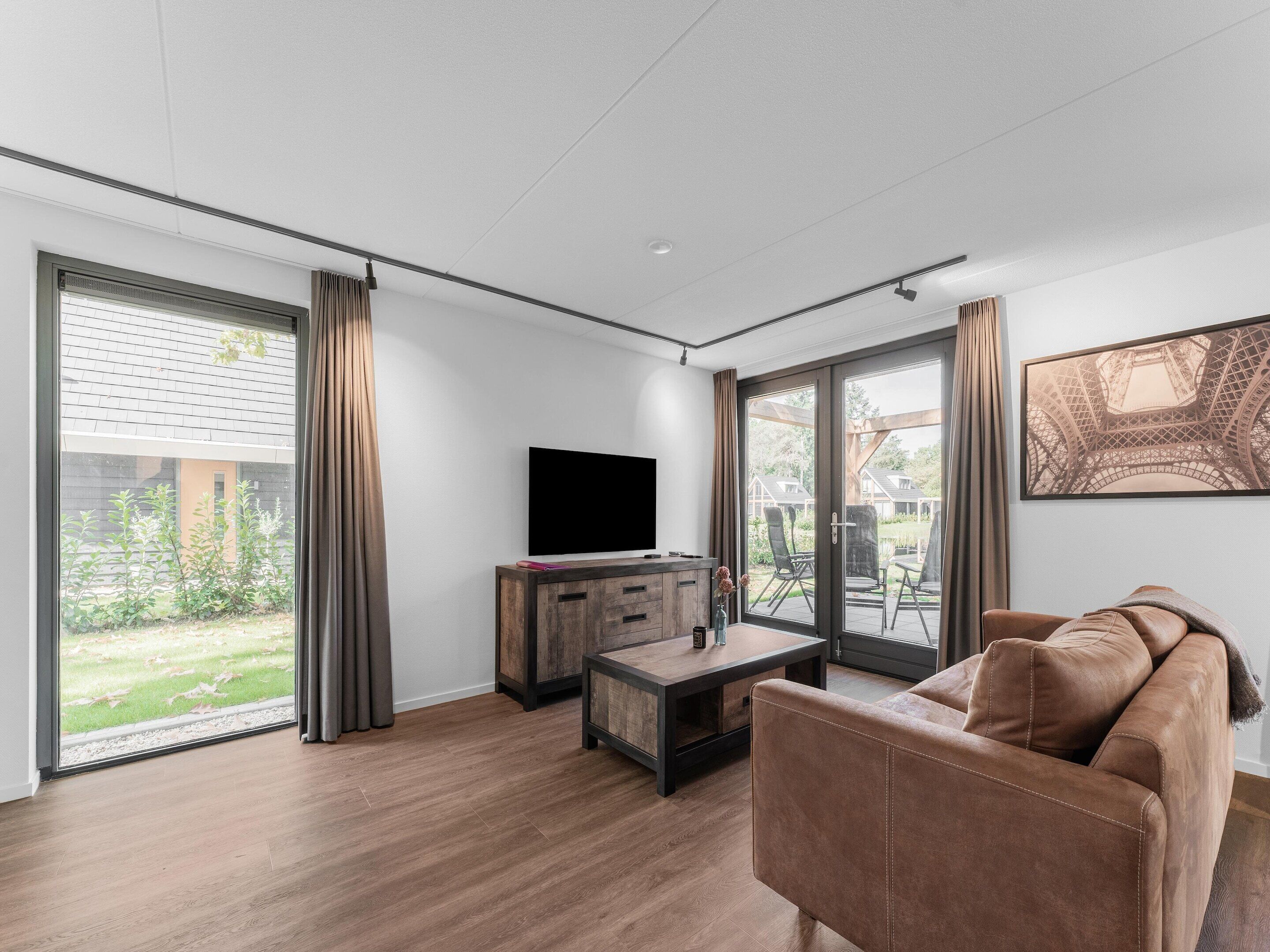 Ein modernes Wohnzimmer mit einem großen Schiebeglastür, einem Flachbildfernseher, einer Holzkommode und einem braunen Ledersofa.