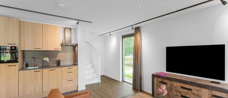 A modern living room with a sofa, a coffee table, and a TV. There is a kitchen area with wooden cabinets and a stove.