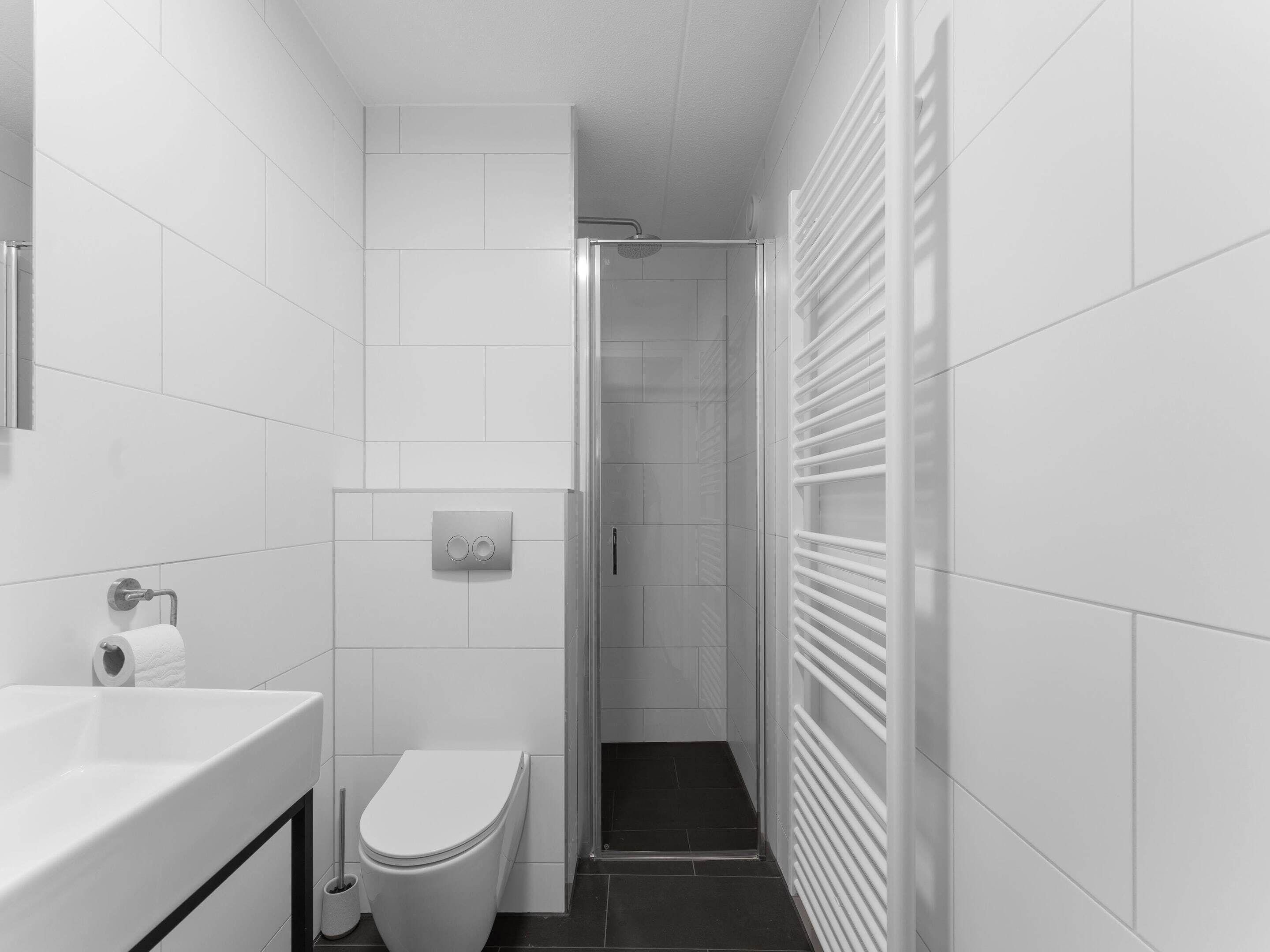 Uma casa de banho moderna com azulejos brancos, sanita, lavatório e zona de duche.