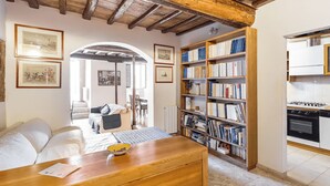 A cozy room with a wooden ceiling, a bookshelf, a dining table, and a kitchen area. - The Balcony Suite -Piazza del Campo View (Siena)