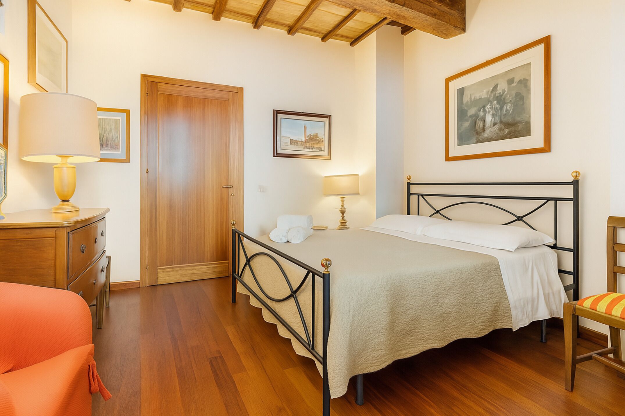 Une chambre à coucher avec un lit, des lampes de chevet, une commode en bois, une chaise et des tableaux encadrés accrochés au mur.