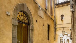 A narrow cobblestone street with a building featuring a wooden door and an arched entrance. - The Balcony Suite -Piazza del Campo View (Siena)
