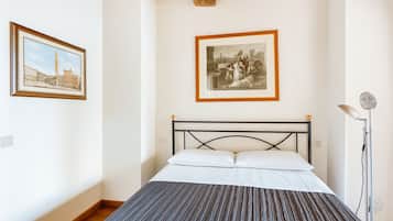 A bedroom with a bed, framed pictures on the wall, and a floor lamp.