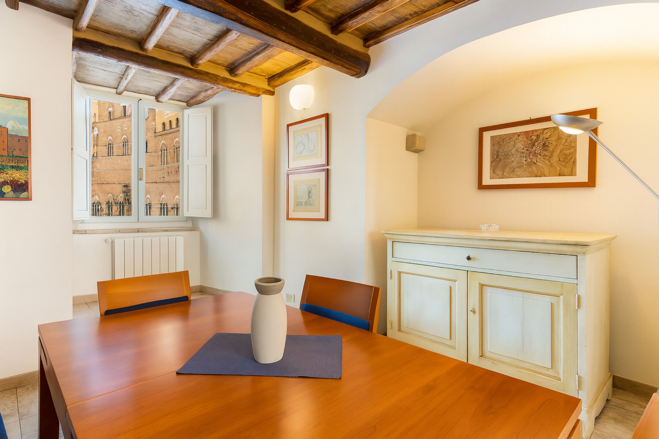 Comedor con mesa de madera, sillas, un jarrón y un aparador.