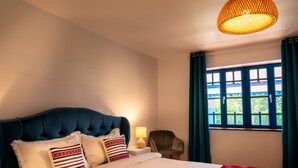 Un dormitorio con una cama grande, una mesita de noche, una lámpara, una silla y una ventana con cortinas.