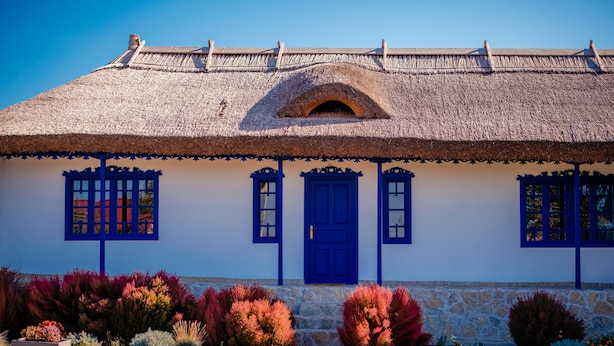 Una casa tradicional con techo de paja, puerta azul y pared de piedra.
