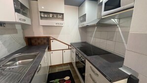 Una cuina compacta amb armaris blancs, un rentapeus d'acer inoxidable, un microones i una placa de cocció.
