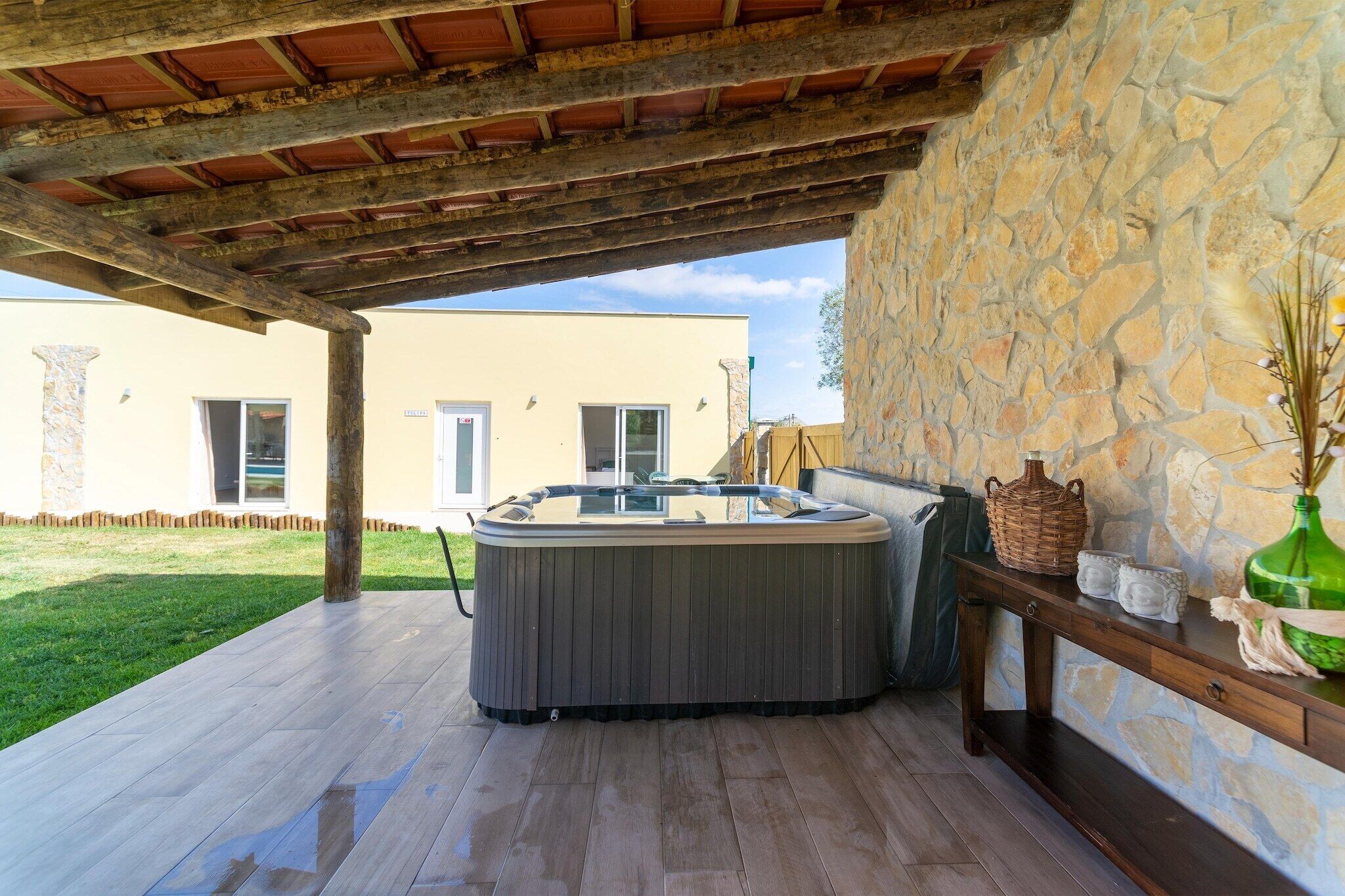 Boblebad under et træbeklædt pergola med en stenvæg og et træbord med pynt.