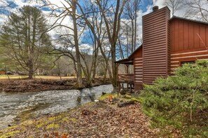 A cabin with a wooden exterior, a river in the foreground, and trees in the background. - A Sweet Retreat | Blue Ridge, GA (Blue Ridge)
