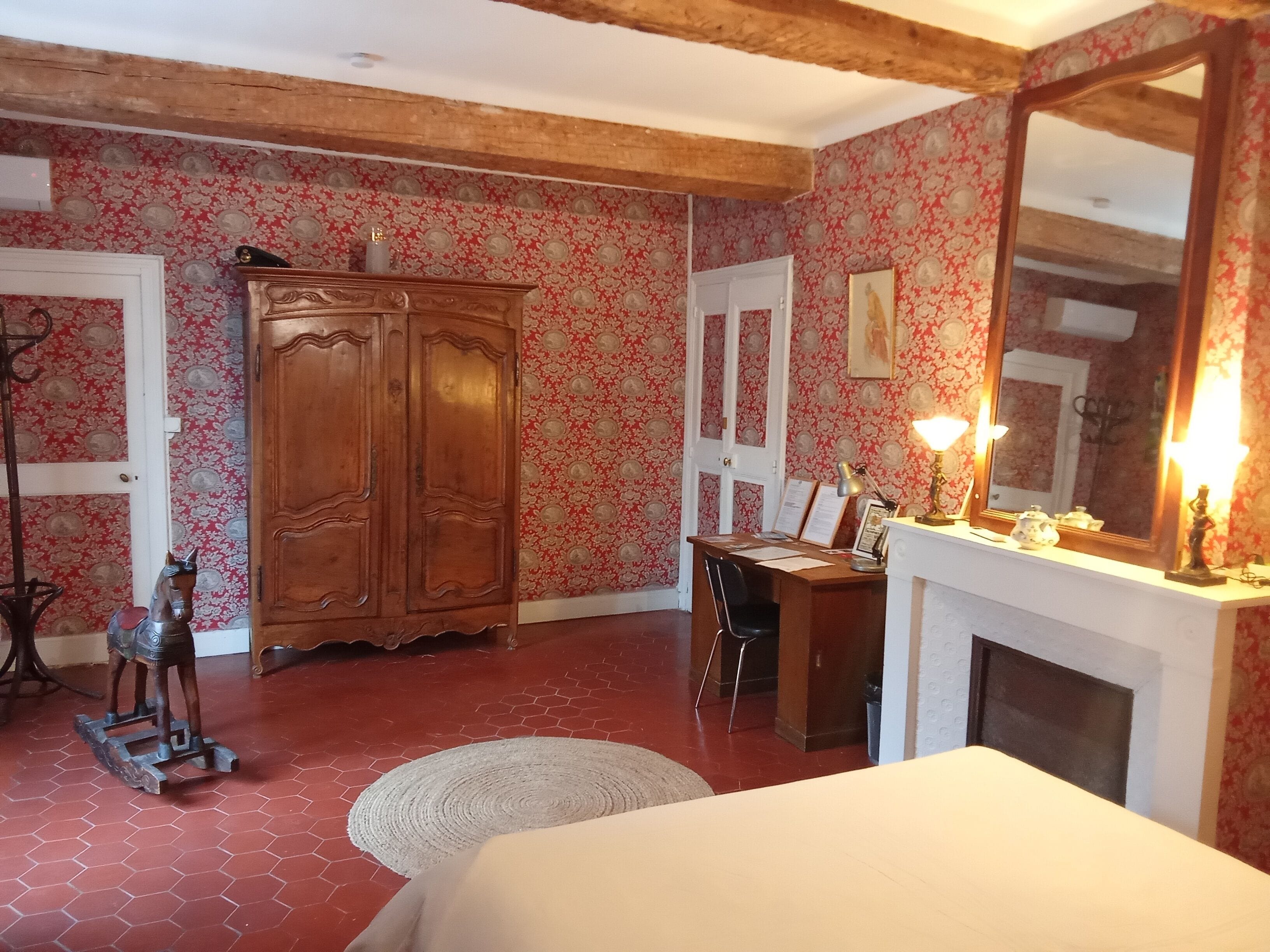 Ein Zimmer mit Holzschrank, Schreibtisch mit Stuhl, Kamin und großem Spiegel.