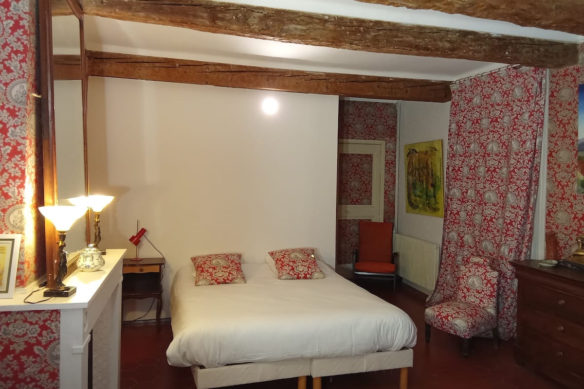 A bedroom with a large bed, a desk with a lamp, a chair, and a wardrobe.