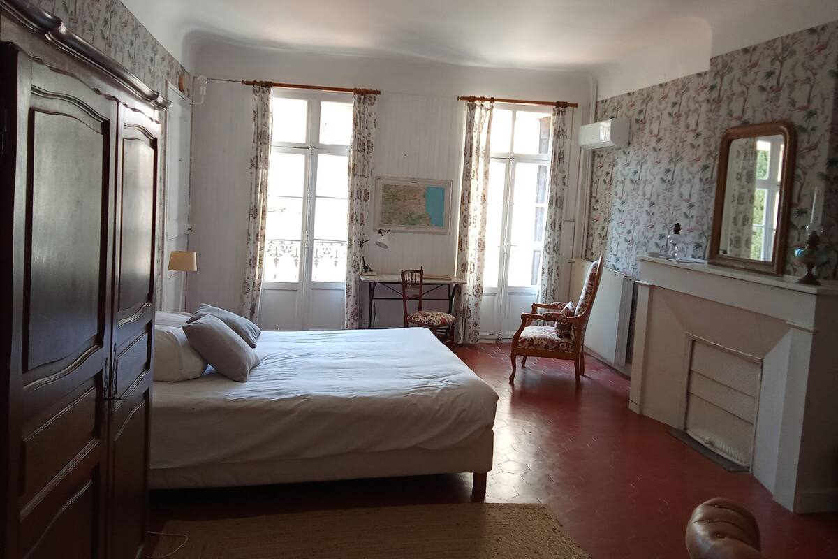 A bedroom with a bed, a desk, a chair, and a fireplace.