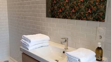 A bathroom with a white sink, two stacked towels, a shower area, and a decorative wall.