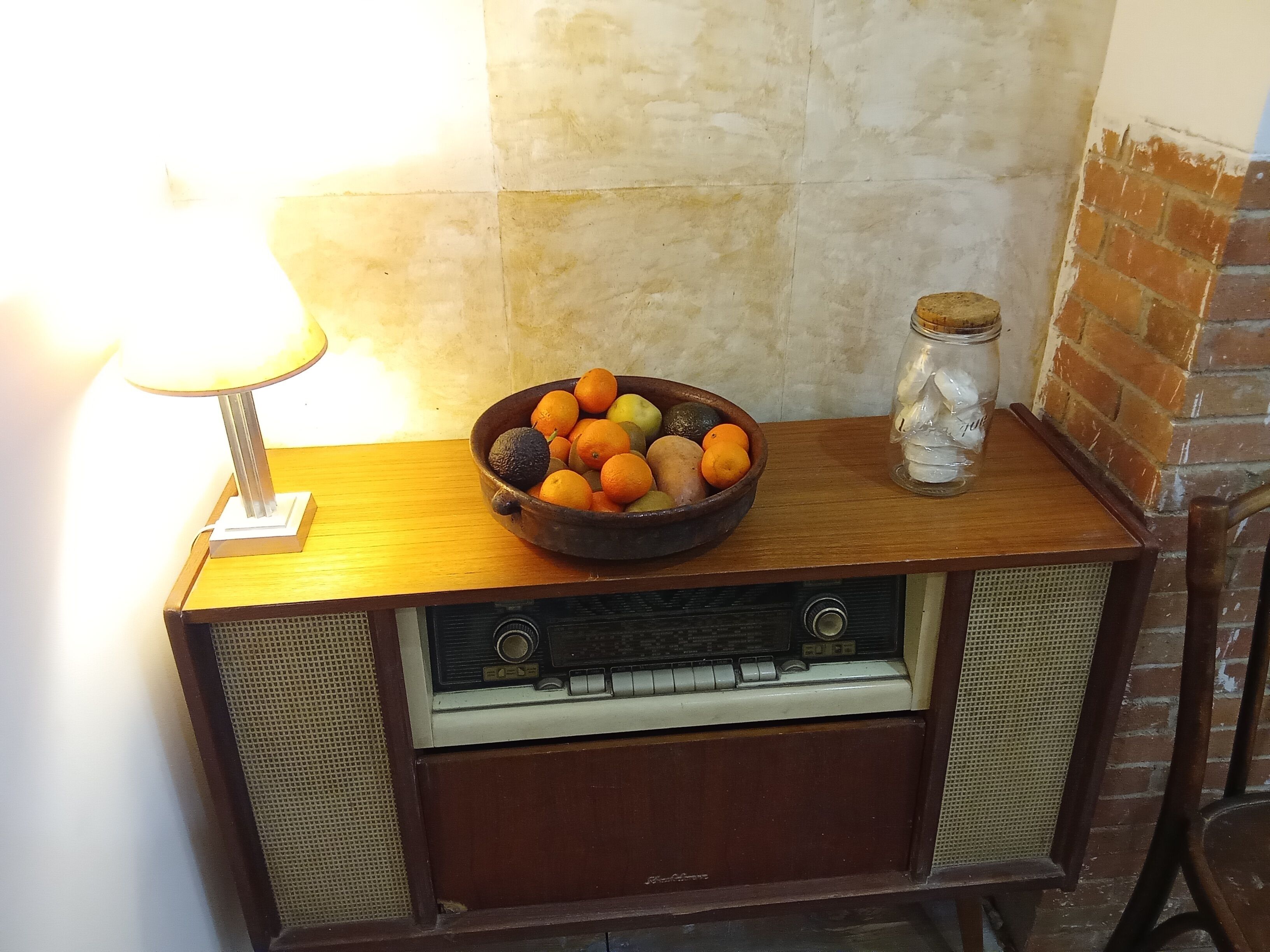 A vintage radio with a bowl of fruit and a jar on top.