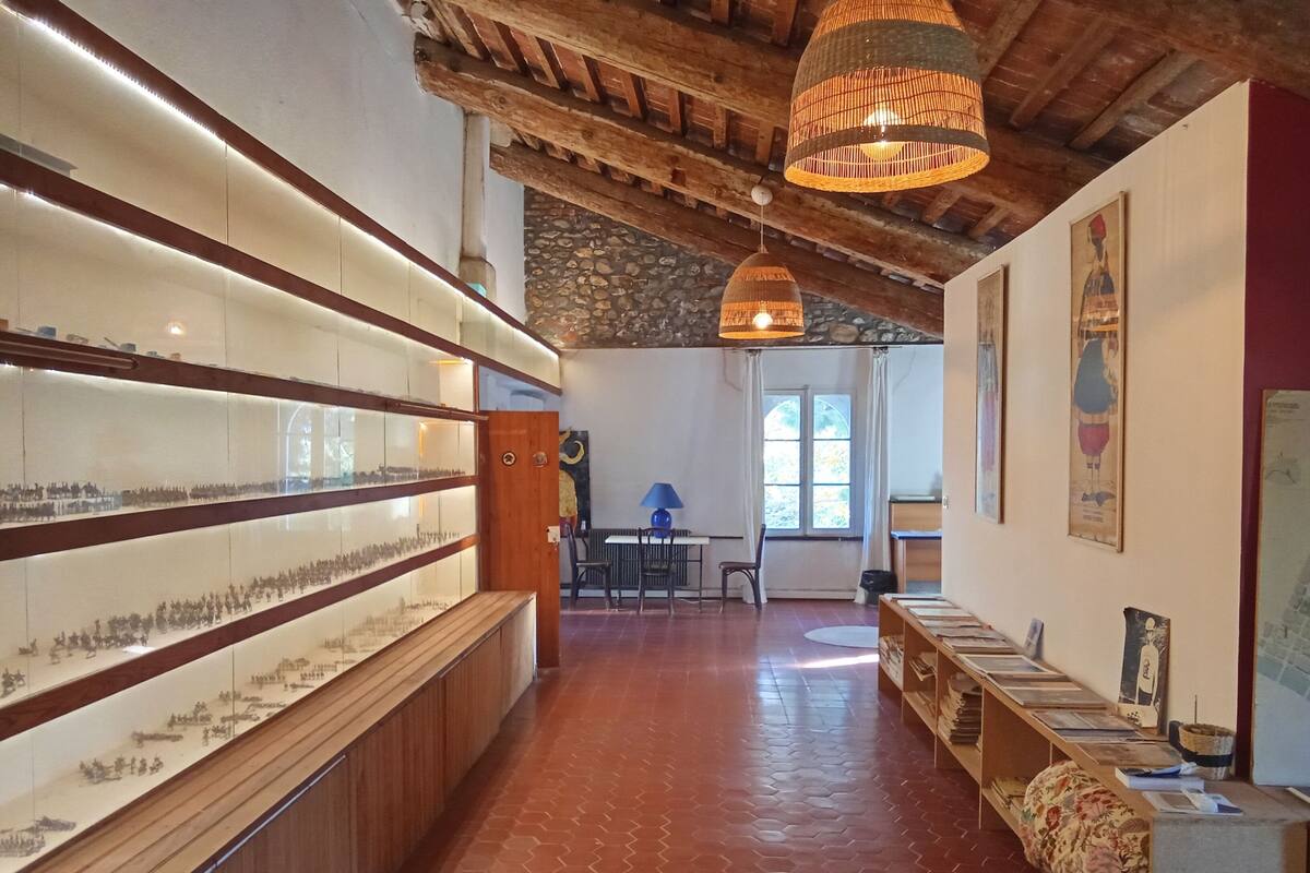 A spacious room with a long wooden display case filled with historical models, a stone wall, and a rustic wooden ceiling.
