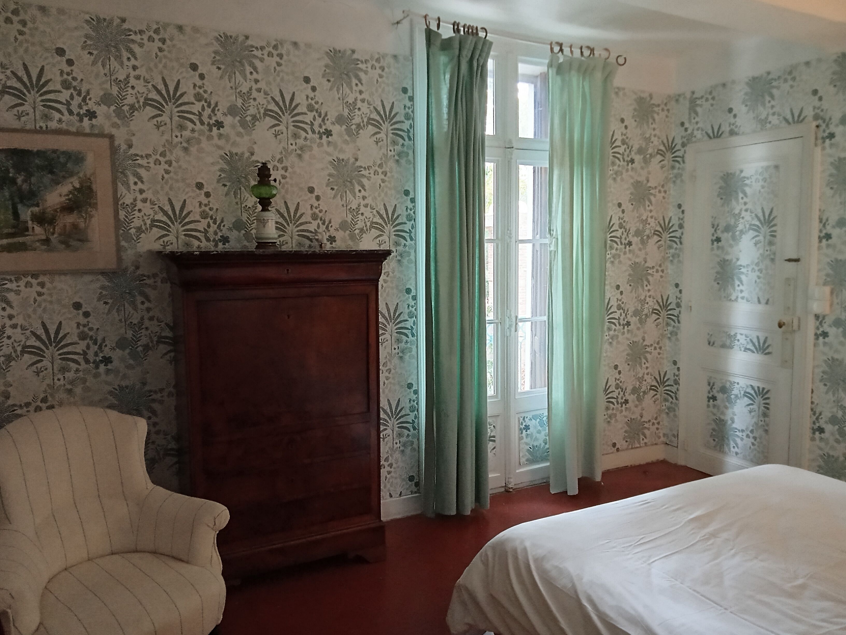 Una habitación con una cama, una silla, un armario de madera y una puerta.