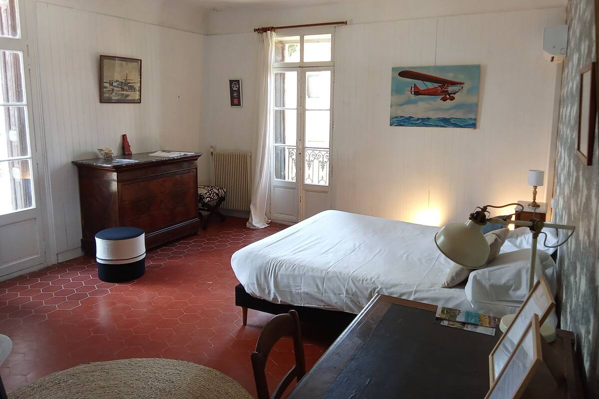 A room with a bed, a desk, a chair, a radiator, and a window with curtains.